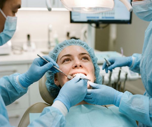 Realistic close-up photo of a young woman wearing a surgical cap during dental treatment, with a team of dentists using dental mirror and tools.
